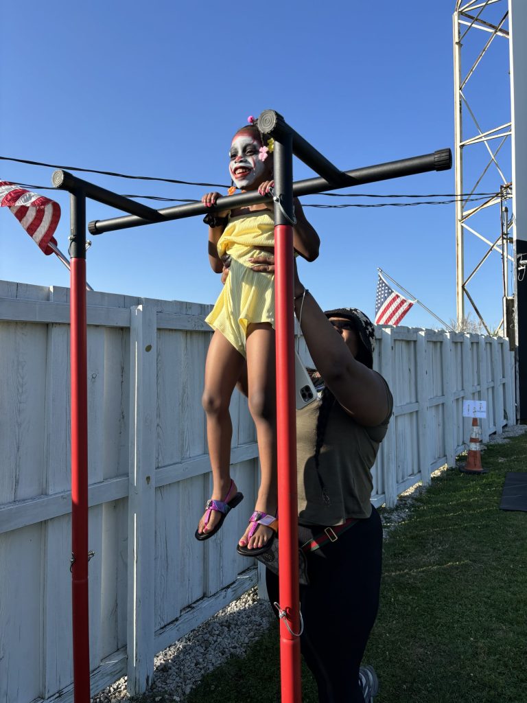 a young girl with her face painted is being held up to the chin up bar by her father