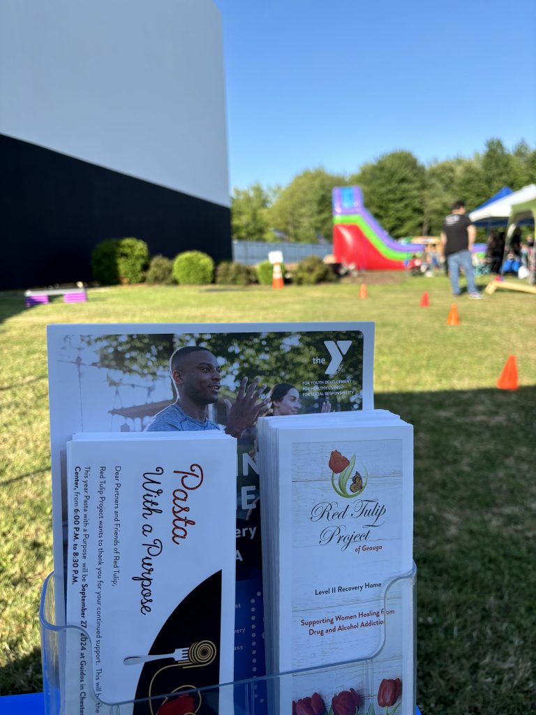 a stand with red tulip project informational materials, in the background is the obstacle course and the drive in movie screen