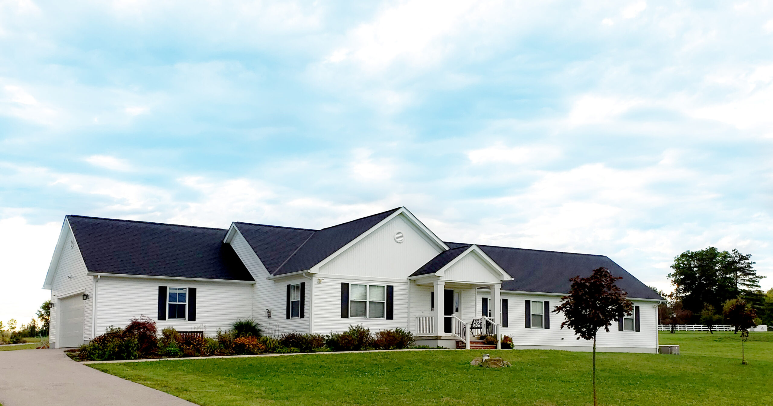 White house with black roof on a green lawn with blue sky
