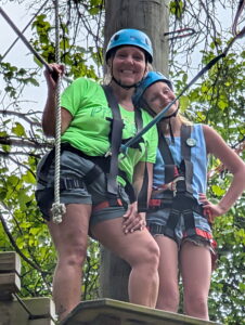 two women in climbing gear posing for photo on the high ropes course